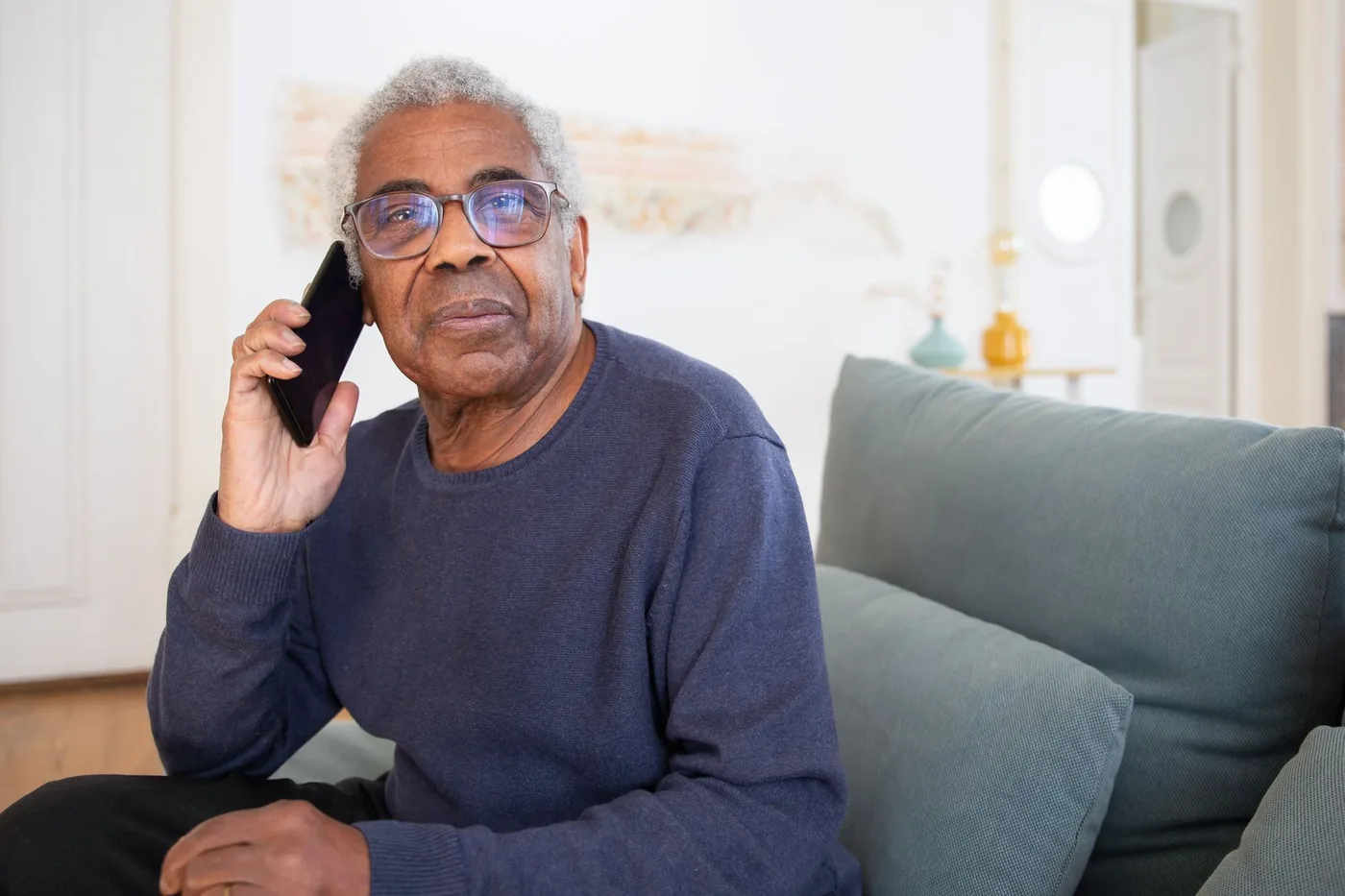 Senior s brýlemi telefonuje na gauči